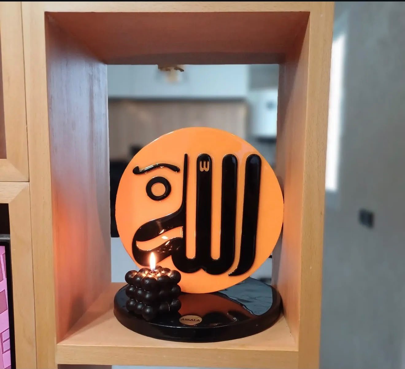 قطعة الله بالألوكوبوند الأسود داخل رفّ خشبي بجانب شمعة مضاءة